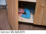 A cheerful toddler baby hides in the closet, his face lighting up with joy as he waits to be found. Inside the old dresser, curious child is hiding, stifling giggles in anticipation. Kid aged 3 years. Стоковое фото, фотограф Андрей Журавлев / Фотобанк Лори