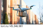 Flying drone delivers package by air in city with residential buildings in background close-up. Стоковое AI-изображение, AI-художник Александр Довянский / Фотобанк Лори