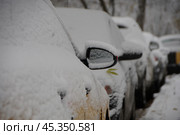 Snow-covered cars are parked in a row by the sidewalk on the street. Стоковое фото, фотограф Ярославский Максим / Фотобанк Лори