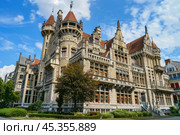 Imposing neo gothic style building with turrets standing tall under blue sky. Стоковое AI-изображение, AI-художник Иван Рябоконь / Фотобанк Лори