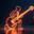 Neon glowing outline of a musician with a guitar on a dark background with a Christmas tree. Стоковое AI-изображение, AI-художник Неведицына Елена / Фотобанк Лори