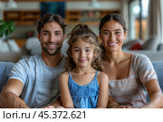 Loving young man hug his beloved wife and little daughter sit on couch in living room, happy people smiling looking at camera posing for photo picture. Exemplary family portrait, love and bond concept. Стоковое AI-изображение, AI-художник Ирина Михайличенко / Фотобанк Лори
