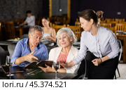 Mature man and woman reads menu and makes order to waitress. Стоковое фото, фотограф Яков Филимонов / Фотобанк Лори