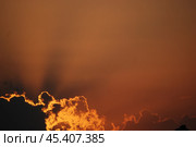 Солнце скрылось за облаком. Солнце склонилось низко к горизонту и спряталось за небольшим количеством облаков. Светило подсвечивает края облаков, и лучи от него расходятся по небу в оранжевых следах. Стоковое фото, фотограф Andrew_Swarga / Фотобанк Лори