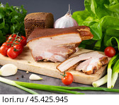 Smoked brisket with vegetables and garlic on a wooden cutting board in a modern kitchen setting. Стоковое фото, фотограф Евгения Трушкова / Фотобанк Лори