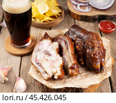 Deliciously cooked pork hooves with a side of crispy chips and a dark drink on a rustic wooden table. Стоковое фото, фотограф Евгения Трушкова / Фотобанк Лори