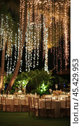 Elegant outdoor wedding reception beautifully decorated with string lights and tables in the evening. Стоковое AI-изображение, AI-художник Юлия Гапеенко / Фотобанк Лори