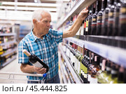 Mature senor choosing alcoholic drinks in supermarket. Стоковое фото, фотограф Татьяна Яцевич / Фотобанк Лори