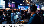 A man wearing headphones sits at a computer and uses a multi-monitor setup to stream a live event for a large audience in a dimly lit conference room. Стоковое AI-изображение, AI-художник Сергей Толмачёв / Фотобанк Лори