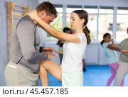 Tween girl performing knee strike in midsection to instructor in self-defense sparring. Стоковое фото, фотограф Яков Филимонов / Фотобанк Лори