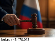 The judge's hand with the judge's hammer on the background of the Russian flag. Стоковое AI-изображение, AI-художник RamA / Фотобанк Лори