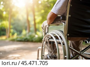 Senior person in wheelchair enjoying freedom walking on road in spring city park outdoor. Old happy man in chair for people with disability has a hope. Disability disease rehabilitation. Close up view. Стоковое AI-изображение, AI-художник Sergey Grishin / Фотобанк Лори