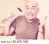imposing man in prime of life holds in teeth of screws and holding hammer. Стоковое фото, фотограф Татьяна Яцевич / Фотобанк Лори