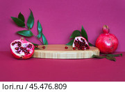 Beautiful composition with ripe pomegranates and pomegranate tree leaves on wooden podium on burgundy background. Can be used as pedestal for presentation of cosmetics with fruit extracts. Стоковое фото, фотограф Виктория Катьянова / Фотобанк Лори
