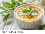 Delicious creme brulee decorated with mint leaves in a white ramekin. Стоковое AI-изображение, AI-художник Юрий Поздников / Фотобанк Лори