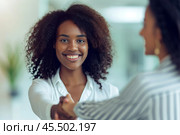 A young African American woman extends her hand for a friendly handshake, warmly welcoming a client in a bright office, reflecting professionalism and approachability. Стоковое AI-изображение, AI-художник Sergey Grishin / Фотобанк Лори