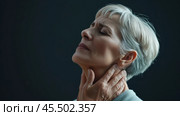 A mature woman is seen in a side view, visibly experiencing neck pain and gently cradling her neck. The photograph emphasizes the emotional and physical toll of discomfort. Стоковое AI-изображение, AI-художник Sergey Grishin / Фотобанк Лори