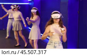 Group of excited young girls standing with handheld controllers in hands engaged in virtual world experiencing through VR glasses covering face. Concept of immersion and interactivity in game. Стоковое видео, видеограф Яков Филимонов / Фотобанк Лори