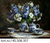 "Magic fountain" of beautiful delphiniums near the tea set. Стоковое AI-изображение, AI-художник Сергей Елизарьев / Фотобанк Лори