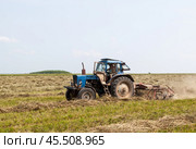 "Agricultural machinery in dusty field", "Tractor working on farmland", "Spring cultivation process", "Rural farming scene", Синий трактор с ворошилкой ворошит сено. Стоковое фото, фотограф Сергей Расторгуев / Фотобанк Лори