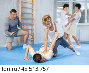 Concentrated boy learning effective self defence techniques in sparring, practicing painful pronating wristlock on male opponent lying face down on floor at sports studio. Стоковое фото, фотограф Яков Филимонов / Фотобанк Лори