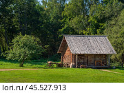 A log outbuilding and an ancient cart on the territory of the Pushkin village Bugrovo of the Pushkin Museum-Reserve on a sunny summer day, Pushkinskiye Gory, Pskov region, Russia. Редакционное фото, фотограф Ula Ulachka / Фотобанк Лори