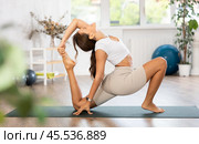 Young woman yoga trainer performing crescent lunge pose on black rug. Стоковое фото, фотограф Яков Филимонов / Фотобанк Лори