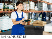 In warehouse of store, guy checks quantity of goods and receipt documents for products. Стоковое фото, фотограф Яков Филимонов / Фотобанк Лори