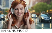 Redhead woman listens to music on headphones while walking along urban city streets on blurred background. Audio book, travel guide or podcast while traveling. Adult girl smile portrait. Panorama. Стоковое AI-видео, аниматор Igor Tichonow / Фотобанк Лори