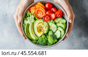 Fresh vegetable bowl filled with vibrant ingredients in hands against a neutral background. Стоковое AI-изображение, AI-художник Сергей Толмачёв / Фотобанк Лори