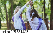 Two girls in purple sashes cheerfully raise their arms in celebration on their final day of school. Стоковое фото, фотограф Mikhail Davidovich / Фотобанк Лори