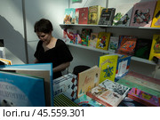 06.04.2023, Москва. Международная ярмарка интеллектуальной литературы «non/fictioNвесна» в Гостином дворе. Девушка среди книг на прилавке. Редакционное фото, фотограф Дмитрий Киселёв / Фотобанк Лори