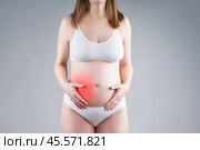 Pregnant woman with abdominal pain, risk of premature birth, gray background. Стоковое фото, фотограф Станислав Тарко / Фотобанк Лори