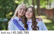 Two jubilant graduates in purple sashes and bow ties share a hug on their final day of school, commemorating the end of a chapter. Стоковое фото, фотограф Mikhail Davidovich / Фотобанк Лори