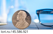 Moscow December 03 2024. Coin on wooden desk with picture of Alfred Nobel, Reading glasses in background. blurred background, Nobel Prize concept. Nobel Prize in Chemistry concept. Редакционное фото, фотограф Скрипачев Антон / Фотобанк Лори
