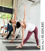 Sporty young female practicing Extended Side Angle Pose Utthita Parsvakonasana on mat on one leg during yoga exercise for balance in group. Стоковое фото, фотограф Яков Филимонов / Фотобанк Лори
