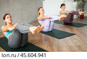 Focused active women balaning in sitting boat posture Paripurna Navasana while training together in yoga center. Стоковое фото, фотограф Яков Филимонов / Фотобанк Лори