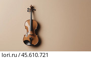 Elegant wooden violin mounted on a smooth beige wall in a minimalist setting during daylight. Стоковое AI-изображение, AI-художник Сергей Толмачёв / Фотобанк Лори