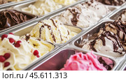 Chocolate, vanilla, strawberry ice cream tubs. Freshly churned various ice cream in a metal containers. Freezer full of icecream in the boxes in cooled counter. Gelato display of many flavors. Стоковое AI-изображение, AI-художник Марина Демидюк / Фотобанк Лори