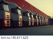 Red trucks parked at a bustling logistics hub area in a row. Lineup of several trucks in the truck parking fully prepared, ready for deliveries. Van transportation truck park. Warehouse distribution. Стоковое AI-изображение, AI-художник Марина Демидюк / Фотобанк Лори