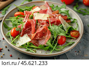 Delicious salad with arugula, coppa, tomatoes and parmesan cheese on gray background. Стоковое AI-изображение, AI-художник Иван Рябоконь / Фотобанк Лори