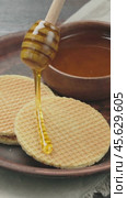 Drops of honey slowly flowing from a wooden honey dipper into a honey bowl, close-up. Honey flowing from a wooden honey dipper on to holland waffles. Vertical video. Стоковое видео, видеограф Андрис Салминьш / Фотобанк Лори