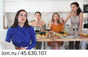 Young dark-haired woman looking hurt and upset during argument with female friends sitting at table in background showing disapproval and discontent during home party. Стоковое видео, видеограф Яков Филимонов / Фотобанк Лори