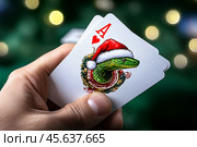 Карты в руке, туз черви с изображением зеленой змеи в красной шапочке Санты. Удача в новом, 2025 году. Стоковое AI-изображение, AI-художник Щеголева Ольга / Фотобанк Лори