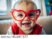 A cute little girl in stylish red heart-shaped glasses, having fun celebrating Valentine's Day. Стоковое AI-изображение, AI-художник Photojuli / Фотобанк Лори