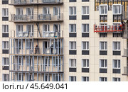 ANGARSK, IRKUTSK REGION, RUSSIA - October 08, 2024: Builders work on high-rise residential building: tiling facade and glazing balconies. Housing construction concept. Modern construction technologies. Редакционное фото, фотограф Виктория Катьянова / Фотобанк Лори