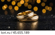 Gold wedding rings on a black background with a side. Wedding rings. The wedding day. The newlyweds. Стоковое AI-изображение, AI-художник Photojuli / Фотобанк Лори