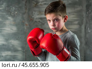 A boy in boxing gloves strikes, a cute teenage boy stands in a fighter's pose, ready to fight. Playing sports. Children's sports sections. Стоковое AI-изображение, AI-художник Photojuli / Фотобанк Лори