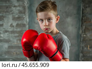 A boy in boxing gloves strikes, a cute teenage boy stands in a fighter's pose, ready to fight. Playing sports. Children's sports sections. Стоковое AI-изображение, AI-художник Photojuli / Фотобанк Лори