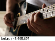 Playing the guitar. Strumming acoustic guitar. Musician plays music. Man fingers holding mediator. Man hand playing guitar neck in dark room. Unrecognizable person rehearsing, fretboard close-up. Стоковое фото, фотограф Марина Демидюк / Фотобанк Лори